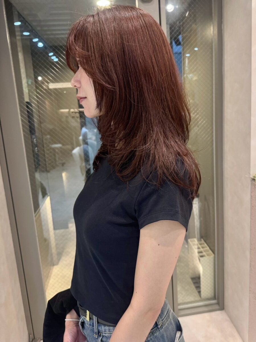 赤みブラウンカラーで艶めくミディアムレイヤーヘアの横顔